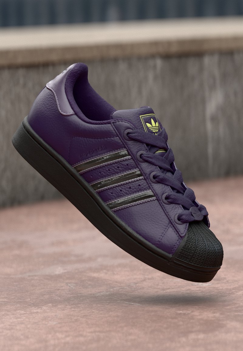 Lilla nahast sneaker musta kummist varvasetükiga, mustade triipude ja sobivate paeltega. Tekstureeritud pind, millel on õmblemisega disain.
