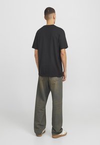 Camiseta de algodón negra, de corte relajado, con mangas cortas. Combinada con jeans de pierna ancha y desgastados, y zapatillas de color claro.