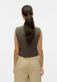 Oliwkowa krótka bluzka ze strukturą ramion, gładką teksturą i dopasowanym tyłem. Połączona z jasnobeżowymi spodniami o wysokim stanie.