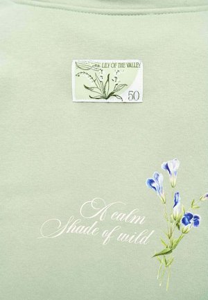 Jasnozielona tkanina z botaniczną naszywką oznaczoną "Konwalia 50", kursywnym napisem "Spokojny odcień dzikości" oraz małymi fioletowymi kwiatami.