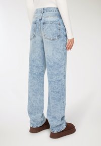 Jeans a gamba larga in denim blu sbiadito con vita media, tasche posteriori e orli grezzi, abbinati a scarpe piattaforma marroni.