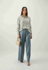Camisa leve com um padrão branco e preto, combinada com calças de cintura alta em azul claro. Uma bolsa bege e sandálias complementam o look.