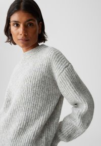Hellgrau gestrickter Pullover mit gerippter Textur, einem hohen runden Ausschnitt und langen Ärmeln. Weiches, lässiges Design, das sich gut zum Layering eignet.