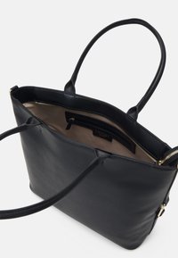 Zwarte leren schoudertas met lange handvatten, ritsluiting en een beige binnenvoering. Bevat een zak en subtiele merkuitingen op de voering.