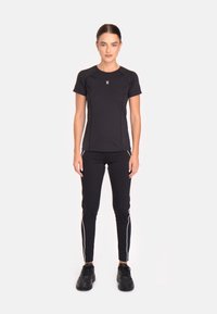 Melnas sportiskas īsām piedurknēm T-krekls ar pieguļošu dizainu un baltu akcentu šuvēm, kombinēts ar melnām legingām ar baltām sānu svītrām un melnām kedām.