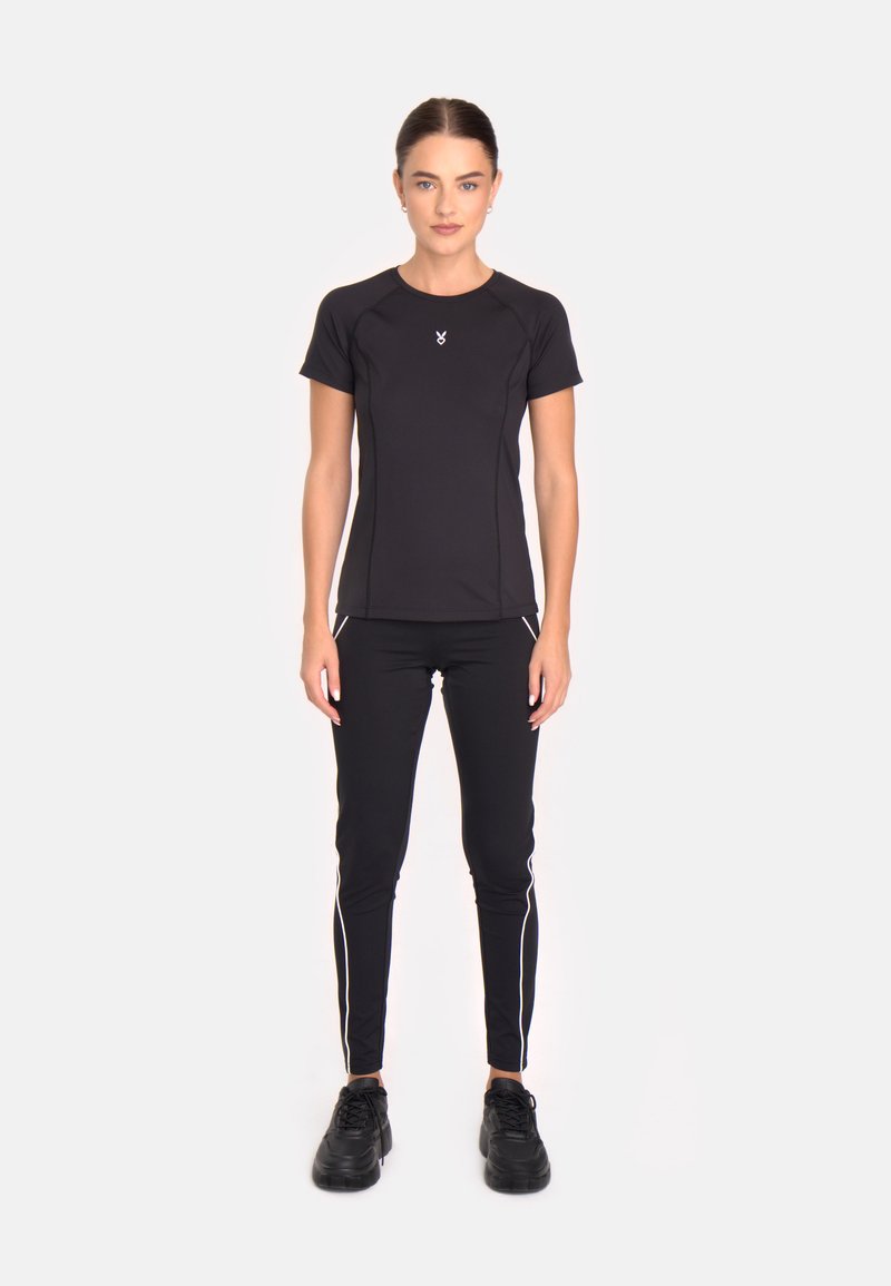 Melnas sportiskas īsām piedurknēm T-krekls ar pieguļošu dizainu un baltu akcentu šuvēm, kombinēts ar melnām legingām ar baltām sānu svītrām un melnām kedām.