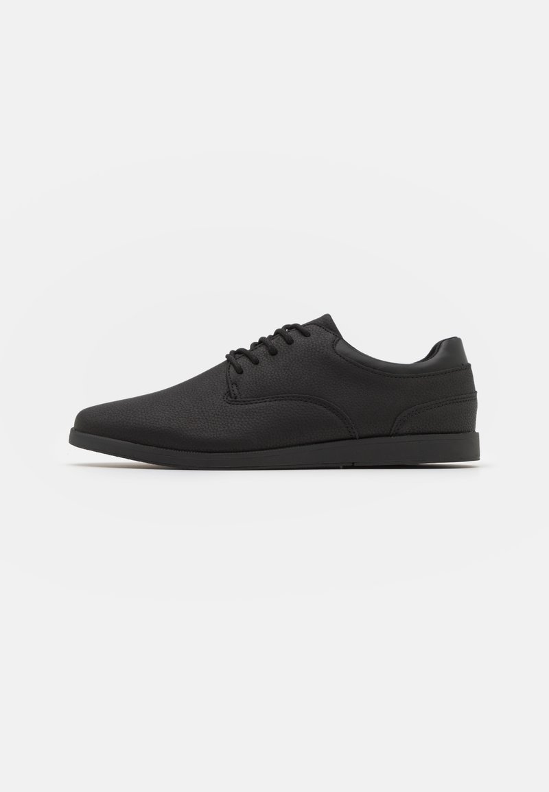 Chaussure habillée noire en cuir à lacets avec un petit talon, un bout rond et des coutures minimales, vue de profil.