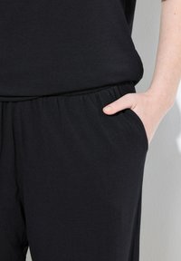 Zwarte loungewear set met een losvallend top en elastische taillebroeken. Stijlvolle textuur met zijzakken, ontworpen voor comfort.