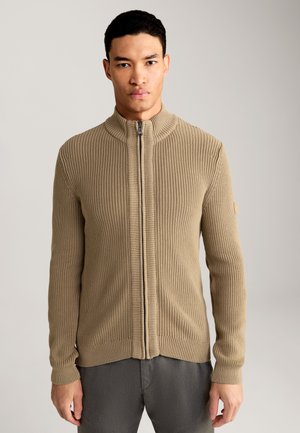 Beige ribbelgebreide trui met een hoge kraag, ritsluiting en lange mouwen; heeft een gestructureerde stof en elastische manchetten bij de polsen.