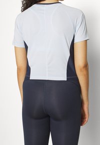 Ljusblå kortärmad träningströja med ett strukturerat mönster, ihop med mörkblå leggings. Tröjan har en figurnära passform med en avklippt längd.
