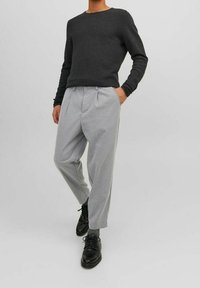 Grå veckade byxor som matchas med en texturerad svart tröja. Outfiten har en avslappnad passform och svarta läderskor.