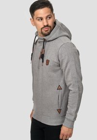 Sweat à capuche gris avec fermeture éclair sur le devant, doté d'une capuche avec cordon, d'accents en cuir et de détails triangulaires sur les côtés. Texture douce.