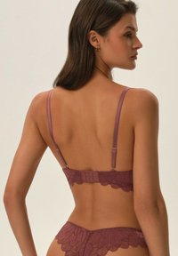 Koronkowy biustonosz w kolorze przykurzonego różu, z regulowanymi ramiączkami, falbaniastymi brzegami i zapięciem na hak i oczko z tyłu; w komplecie z pasującymi majtkami.