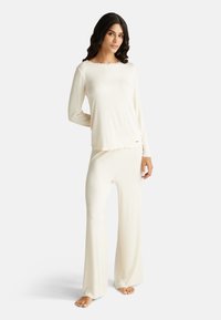 Krémová žebrovaná souprava na volný čas zahrnující dlouhý rukáv s výstřihem do vlny a odpovídající rozšířené kalhoty, vyrobená z měkké, lehké látky.