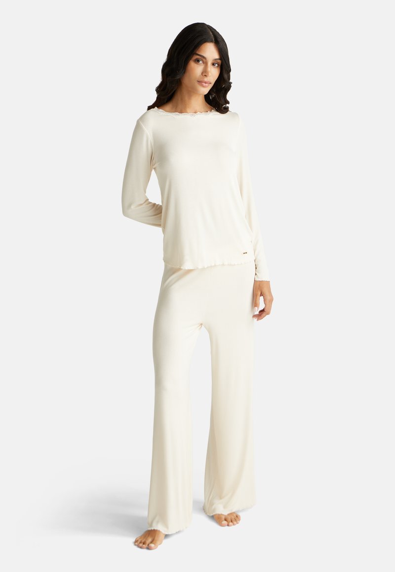 Krémová žebrovaná souprava na volný čas zahrnující dlouhý rukáv s výstřihem do vlny a odpovídající rozšířené kalhoty, vyrobená z měkké, lehké látky.