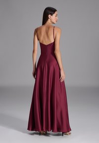 Robe de soirée satinée marron avec de fines bretelles, un dos décolleté et une jupe fluide. Équipée d'une fermeture éclair et d'une texture lisse.