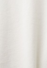 Bílá látka s hladkým, texturovaným povrchem, vykazující jemný tkaný vzor. Lehkým způsobem zavěšená, vytvářející měkké, plynulé záhyby.