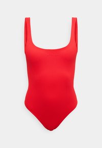 Punane üheosaline ujumistrikoo laiade õlarihmadega ja õrn Calvin Kleini logo rinnal, esitletud ühevärvilise tausta ees.