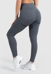 Gray ribbed leggings with a high waistband and contoured back. Paired with white sneakers featuring a visible air cushion.
