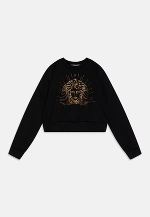 Sudadera negra corta con mangas largas que presenta un gráfico en relieve dorado de una cara y líneas radiales. Tejido suave, cuello redondo.