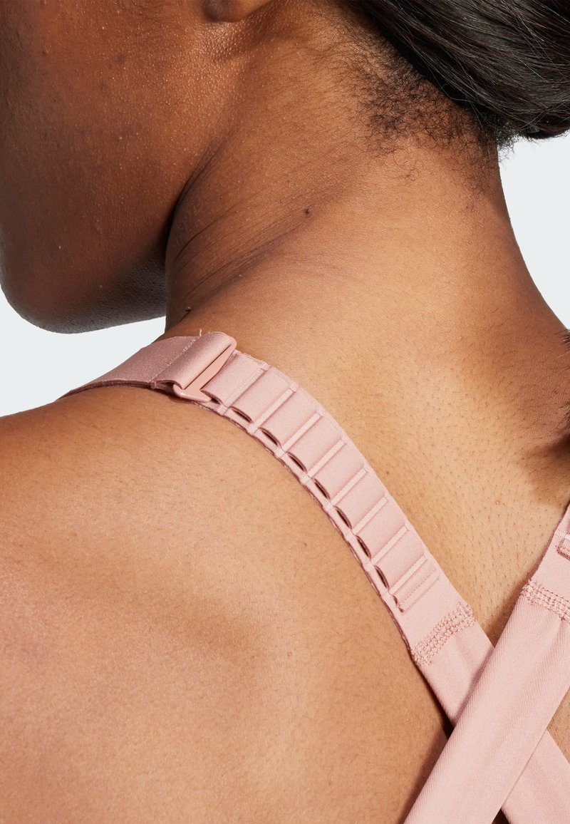 Weicher pinker BH-Träger mit verstellbarem Zubehör, aus glattem Stoff mit strukturierter Oberfläche, kreuzt sich auf der Haut am Nacken.