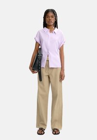 Jasnofioletowa koszula z krótkim rękawem na guziki, beżowe szerokie spodnie, czarna torebka na ramię oraz czarne sandały na obcasie z ozdobnymi detalami.