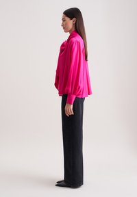 Blusa di seta fucsia con scollatura drappeggiata e maniche lunghe, abbinata a jeans neri a gamba dritta a vita alta e scarpe nere a punta.