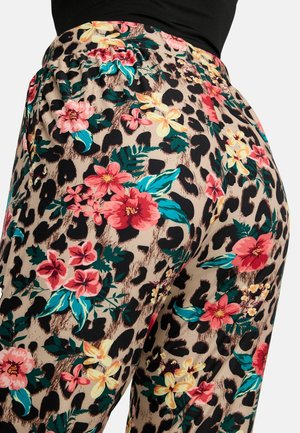 Pantaloni cu imprimeu floral și leopard în bej, negru, roșu, galben, verde teal și verde, purtați cu un top negru.