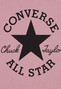 Rožinė medžiaga su didele juoda žvaigžde centre, o viršuje tekstas "CONVERSE" ir apačioje "Chuck Taylor ALL STAR" kontrastingais šriftais.