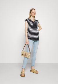 Camiseta listrada azul-marinho e branca, jeans skinny azul-claro, bolsa de alça trançada e sandálias bege. Design minimalista com um ajuste descontraído.