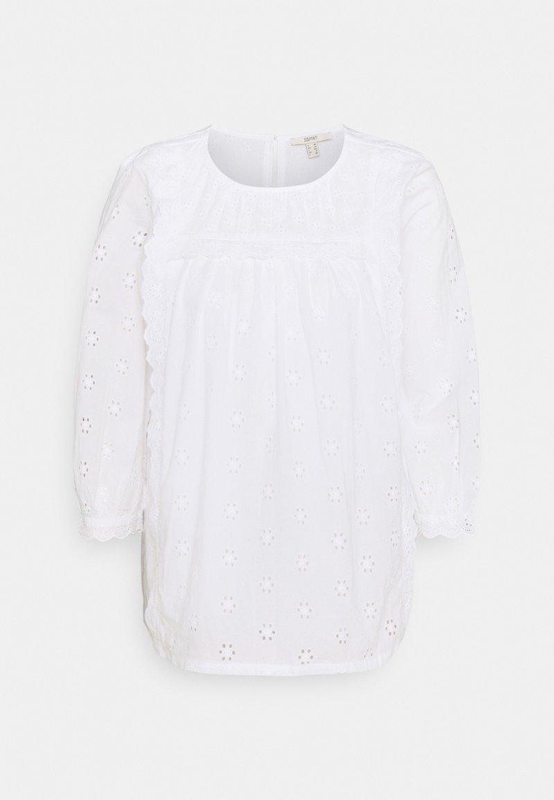 Blouse blanche à manches longues avec col rond, broderie florale à jours, bordure festonnée sur le devant et les poignets, fermeture éclair au dos.