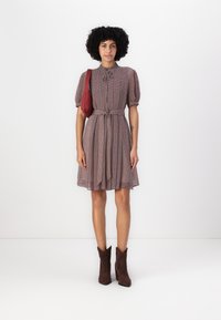 Rochie cu un model roșu și alb, cu mâneci tip balon, talie strânsă și guler cu nasturi. Asortată cu cizme brown la gleznă și o geantă roșie.