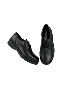 Zapatos de cuero negro con punta redonda, cierre de cordones al frente y suela gruesa de goma. Presentan detalles de costura a lo largo de la parte superior.