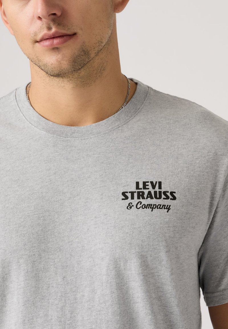T-shirt gris à manches courtes en coton. Présente un logo imprimé noir "LEVI STRAUSS & Company" sur le devant, avec un col rond.