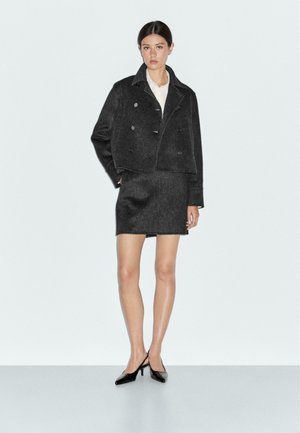 Black cropped wool jacket with a double-breasted design, paired with a matching pencil skirt. Model wears a white shirt and black heels.