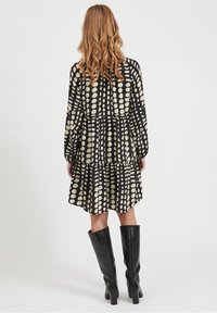 Sort og beige kjole med lagdelt design, prydet med et pletmønster og lange ærmer. Kombineret med knæhøje sorte støvler.