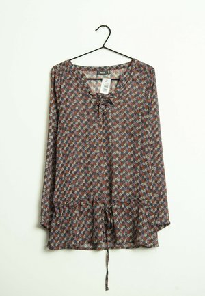 Blusa de manga larga con estampado floral, escote con cordones y cintura con cordón ajustable, colgada en una percha negra sobre fondo blanco.