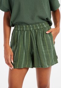 Shorts verts en tissu texturé, avec des rayures verticales de pois blancs et jaunes. Taille élastique et poches latérales.
