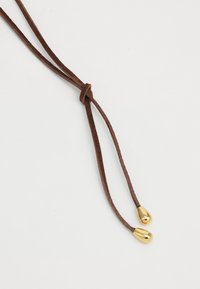 Corda in suede marrone con due estremità metallizzate dorate, caratterizzata da un finish liscio e una forma a goccia allungata, fissata con un nodo.