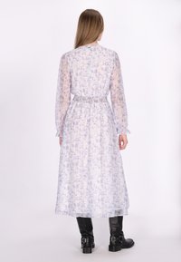 Langes, hell-lavendelfarbenes Kleid mit Blumenmuster, elastischem Bund und langen Ärmeln. Tragen mit schwarzen Knöchelstiefeln. Halbtransparenter Stoff und fließendes Design.