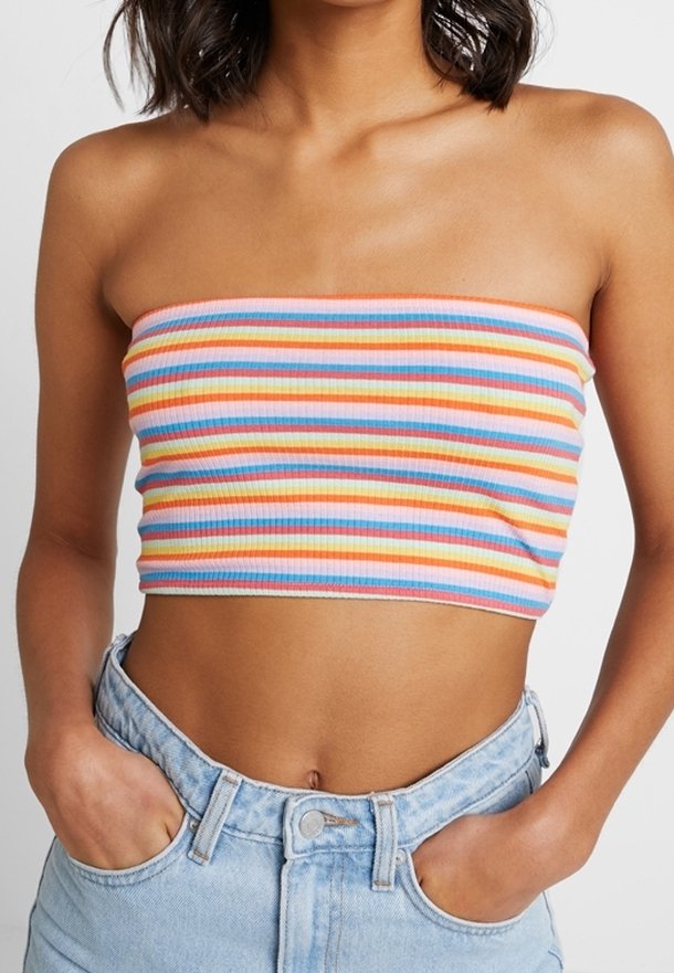 Persoon in een kleurige horizontaal gestreepte tube-top en lichtblauwe high-waisted jeans met handen in de zakken, torso zichtbaar.