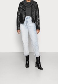 Svart läderbikerjacka över en grå tröja, i kombination med ljusblå högmidjade jeans och svarta ankelboots med mönstrade klackar.