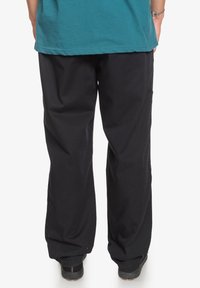 Černé kalhoty s širokými nohavicemi z pevné látky, s pohodlným střihem, hladkou strukturou a bez viditelných vzorů či ozdob.