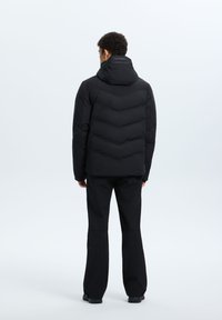 Giacca a vento nera con design a zigzag trapuntato, cappuccio rimovibile e polsini elasticizzati, abbinata a pantaloni neri a sigaretta.