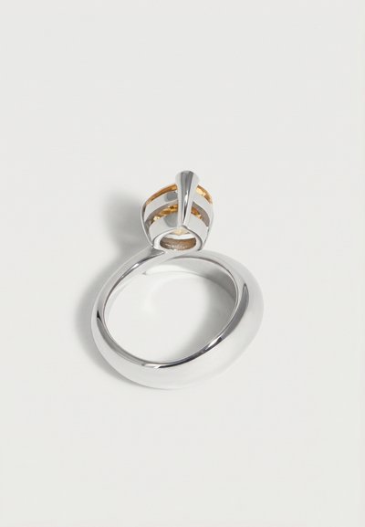Anillo de plata pulida con una banda ancha, que presenta un diseño abierto tipo jaula en la parte superior con acentos dorados dentro de la jaula.