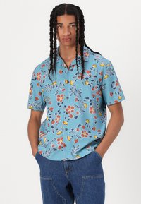Short-sleeve, button-up shirt in light blue with floral and leaf patterns in red, yellow, and navy. Collared with a relaxed fit.