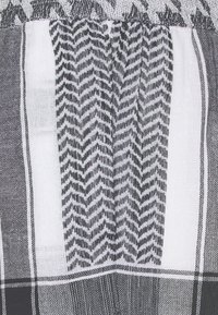 Černobílá tkanina s tkanými geometrickými vzory, včetně cik-cak a kostkovaných designů, s měkkým, texturovaným povrchem.