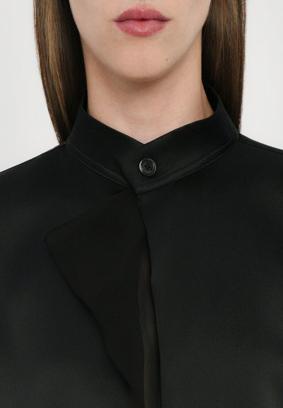 Black blouse with a high collar, featuring a button at the neck. The fabric appears smooth, with a slight sheen and a structured neckline.