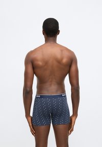 Tengerészkék boxeralsó geometrikus fehér mintával, rugalmas anyagból, és a "BOSS" szó fehér betűkkel díszített márkázott derékpánttal.