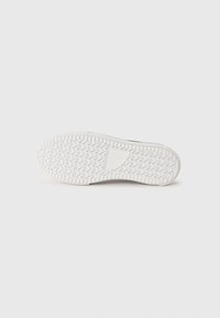 White rubber shoe sole with a zigzag tread pattern, slightly raised edges, and a smooth surface. Minimalistic design with no visible logos.
